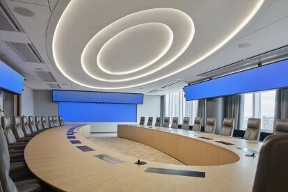 A conference room with large blue screens around a rounded desk, all sitting under an oval-shaped ceiling