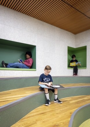 Students sit in cubbies in the wall, while another sits reading on the stairs