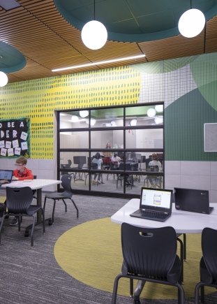 Colorful wall segmented by a garage-type door made of glass. Chairs and desks all around the space.